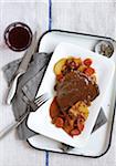 Steak with gravy served with potatoes, carrots and onions and a glass of red wine