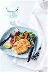 Sesame seed crusted chicken breast with spinach salad and red peppers on a blue plate