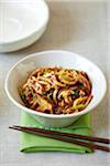 Bowl of udon noodles with shiitake mushrooms, green onions, chili sauce served with chopsticks on a green napkin