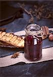 glass jar with raspberry jam on a black background, behind slices of white bread