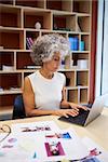 Senior businesswoman working on laptop in office, vertical
