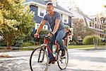 Father Cycling Along Street With Daughter In Child Seat