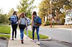 Four young teen girls walking to school together, back view