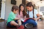 Group Of Children Sit On Porch Of House Reading Books Together