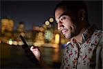 Man Using Mobile Phone At Night With City Skyline In Background