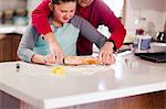 Girl and grandmother rolling cookie dough together at kitchen counter