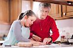 Girl and grandmother using cookie cutter on dough at kitchen counter