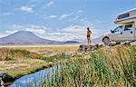 Mature man standing on rock, beside recreational vehicle, looking at view, Salar de Chiguana, Chiguana, Potosi, Bolivia, South America