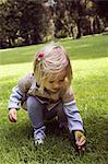 Female toddler crouching to pick dandelion in park