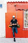 Male hipster leaning against red wall looking at smartphone