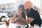 Mature hipster couple lighting cigarette at sidewalk cafe, Valencia, Spain