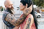 Mature tattooed hipster man with hand in girlfriend's hair