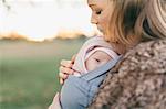 Mother and baby daughter outdoors, mother carrying baby in baby sling