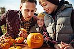 Man with son and daughter looking at carved halloween pumpkin at pumpkin patch