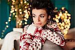Young woman sitting at home, wearing christmas jumper, thoughtful expression
