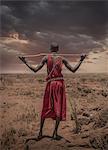 Masai man with traditional dress watching stormy clouds over the savannah, Amboseli, Rift Valley, Kenya