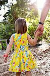 Father and daughter walking outdoors, holding hands, rear view