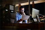 Young businessman reading paperwork at office desk at night