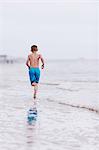 Boy running along water's edge at beach, rear view,  Dauphin Island, Alabama, USA