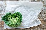 A savoy cabbage on paper and a wooden background (top view)