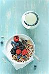 Yoghurt and muesli with berries in a bowl next to a glass bottle of yoghurt