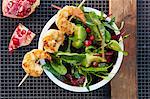 A prawn skewer on avocado salad with pomegranate seeds