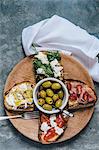 Various bruschettas and olives on a wooden plate