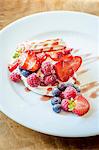 Deconstucted Eton mess with meringue, whipped cream, strawberries, blueberries, raspberries with a berry sauce on a white plate and wooden table