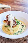 Sea bass fish fillets wrapped in bacon on a potato mash with spinach and chives with a pour of white wine sauce