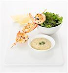 Grilled prawns on a skewer with chilly and pepper, bowl of mixed lettuce, Lemon wedges and tartare sauce with dill topping