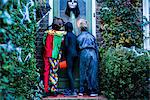 Three boy in halloween costumes, standing at door, trick or treating, rear view