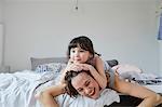 Mother and daughter lying on bed, daughter lying on mother's back