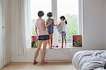 Mother, son and daughter looking out of bedroom window, rear view