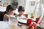 Young boy and girl sitting at dinner table, smiling