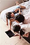 Mother, son and daughter lying on bed, using digital tablet, elevated view