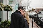 Mid adult couple in street, kissing, holding umbrella