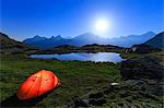 Night of full moon with camping tend on the shore of a small lake. Alpe Fora, Valmalenco, Valtellina, Lombardy, Italy.
