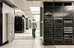 Computer server room racks with technician in background.