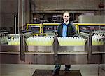 Portrait of a Caucasian male worker standing next to a conveyor belt of lemon flavoured water in a bottling plant.