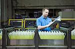 Caucasian male worker checking inventory next to a conveyor belt of lemon flaored water in a bottling plant.