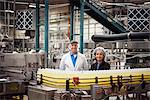 Portrait of a Caucasian male and African American female team of workers wearing head nets and standing near a conveyor belt of lemon flavoured water in a bottling plant.