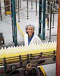 Portrait of African American female worker wearing a head net and standing near a conveyor belt of lemon flavoured water in a bottling plant.