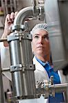 Caucasian female technician wearing a head net and checking large stainless steel processing tanks in a bottling plant. that makes flavoured bottled water.