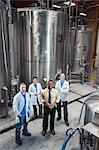 Portrait of a team of Caucasian technicians and an African American management person standing next to large processing tanks in a bottling plant.