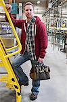 Portrait of a man arriving for work with his toolbag in a warehouse bottling plant.