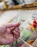 Close up of a hand holding a fly in a fly shop.  The fly is used to catch trout and salmon while fly-fishing.