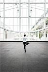 Businessman relaxing doing a yoga pose in a large open glass covered walkway.