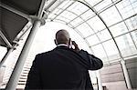 Black businessman on the phone while walking through a large glass covered walkway.