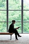 Caucasian businesswoman working on a computer while sitting on a bench in a business centre lobby.