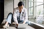 Asian woman doctor working on a lap top in a hospital  hallway.